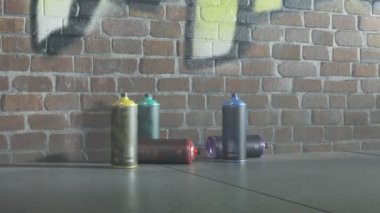 Kırmızı ve mavi polis arabasının ışıkları sprey boya kutularını aydınlatıyor. Çocuk vandalizmi şüphelisi kaçmış ama boya kutularını bırakmış. Kamera yavaş hareket ediyor. Tuğla duvardaki yeni grafitiyi gösteriyor.