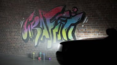Kırmızı ve mavi polis arabasının ışıkları eski tuğla duvarı aydınlatıyor ve üzerinde yeni renkli grafiti etiketi var. Vandalizm şüphelisi kaçtı. Kamera yavaş yavaş üst görüntüye doğru hareket eder ve sokak sanatını gözler önüne serer..