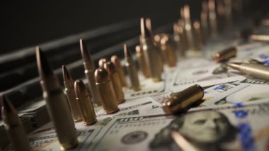 Bir yığın paranın üzerinde duran sayısız mermi. Arka planda nakit para ve yerde dolar. Sonu gelmeyen, kusursuz bir döngü animasyonunda kamera yana hareket ediyor. Zenginlik, güç ve yozlaşma