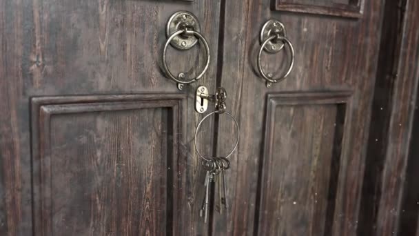 木材で作られた古風なドアを見る ゴールデンロックにキーを1つ入れる この鍵はドアロックを開ける それはまた他の錠のためのキーが付いているリングを保持します ヴィンテージゴールデンドアノッカー — ストック動画
