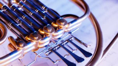 Müzik notaları üzerinde dinlenen bir kornonun yakın plan çekimi. Yavaş kamera hareketleri ve kontrastlı ışıklar. Proffesional orkestra veya bando oyuncuları tarafından kullanılan parlak altın borudan yapılmış pirinç bir enstrüman..