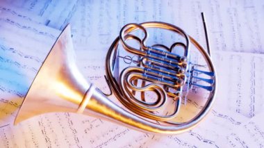 Müzik notaları üzerinde dinlenen bir kornonun yakın plan çekimi. Yavaş kamera hareketleri ve kontrastlı ışıklar. Proffesional orkestra veya bando oyuncuları tarafından kullanılan parlak altın borudan yapılmış pirinç bir enstrüman..