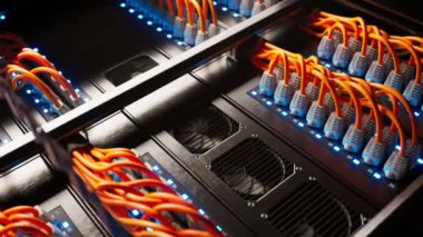 Modern bir sunucu odasındaki sayısız turuncu kablo karanlık bir tarlada tek bir spot ışığıyla aydınlatılıyor. Renkli ethernet kabloları. Sonsuz, kusursuz döngü animasyonu. Perspektif görünümü.