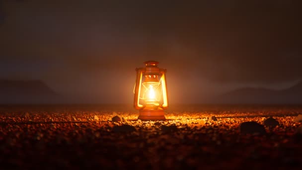 小さな小石に囲まれた砂漠の真ん中に立っている古いヴィンテージランプ 暗闇に希望を与える暖かい炎の光 旅行休憩する 背景にあるヒルズ カメラヘッディング — ストック動画