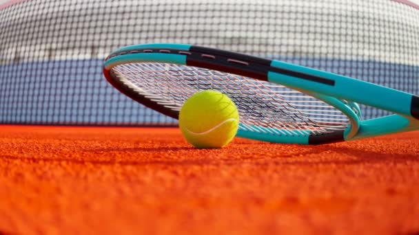 蓝色网球拍 球落在橙色的球场上 背景中的网络 相机转向专业的运动器材 活跃的生活方式在比赛中途 — 图库视频影像