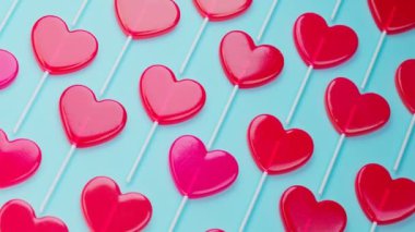 Kırmızı kalp şeklindeki lolipopların kusursuz döngülü animasyonu. Çubuklarda tatlı tatlılar. Aşkın sembolü. Mavi arka planda tatlı çeşitli şekerler. Lezzetli romantik Sevgililer Günü hediyesi.