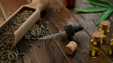 Kenevir ürünleri masada. Kamera tahta kaşıktaki kenevir tohumlarından başlıyor. Sonra cam şişelerdeki gerekli yağlar, marihuana yeşili yapraklar ve bitki. Esrarın kozmetik kullanımı kavramı.