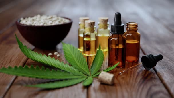 木桌上的大麻油动画 将香精油放在小玻璃瓶中 旁边放有大麻绿叶和大麻籽 大麻的治疗和化妆品用途概念 — 图库视频影像