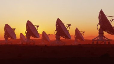 Gün batımında çölde uydu anteni seti. Uzay gözlemevi sinyal araması. Radyo astronomi gözlemevi. Anten siluetleriyle renkli alacakaranlık manzarası. Keşif, bilim, teknoloji.