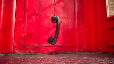 Kırmızı bir telefon kulübesinde asılı siyah bir cep telefonu. İngiliz telefon kulübesi görüntüsü. Asılan ahizenin yere değdiği yere yaklaş. Teknolojik ilerleme kavramı ve iletişimin gelişimi