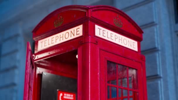 壁に掛かる受信機が付いているイギリスの赤い電話ブースとの映像 ロンドンとイギリスのシンボル バックグラウンドの建物を持つ通りの古いレトロコミュニケーションキオスク 電話を取る — ストック動画