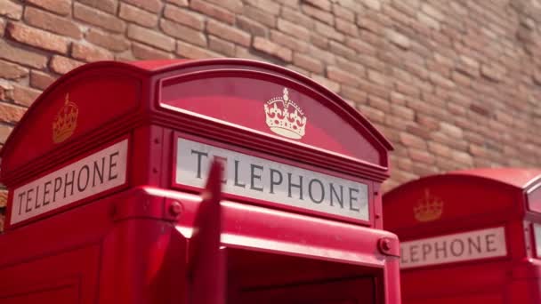イギリスの赤い電話ブースの映像 ロンドンとイギリスのシンボル バックグラウンドの建物を持つ通りの古いレトロコミュニケーションキオスク 黄金の王冠のシンボルと言葉に近づいてください 電話を取る — ストック動画
