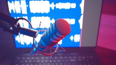 Bir podcast sırasında yakın çekim ses mikrofonunun renkli animasyonu. Mavi ekran kaydındaki DAW ses dalgaları. Kırmızı ve mavi neon ışıklar. Detaylı mikrofon ve şok montajı..