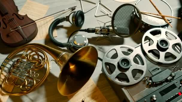 楽器は 古いノートシートと回転テープリール付きのレコーダーを備えた床に配置されています ヴァイオリン ドラム トランペット 三角形 ドラムプレート マイク ミュージシャン解体スタジオ — ストック動画