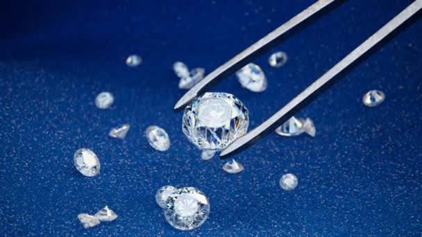 青いベルベットの生地に多くのダイヤモンド 一つは 最大のダイヤモンドは 金属の宝石のツイーザーのペアによって選ばれています ラグジュアリージュエリー作り 光沢のある 高価で貴重な素晴らしいプレゼンテーション 4Kについて — ストック動画