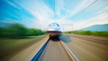 Hızlı, modern bir tren dağlık bir arazide hızla ilerliyor, büyük bir hızla ilerliyor. Ön taraftan vurulmuş. Trenin yanından bir sürü ağaç ve çalılığın geçtiği güneşli bir gün..