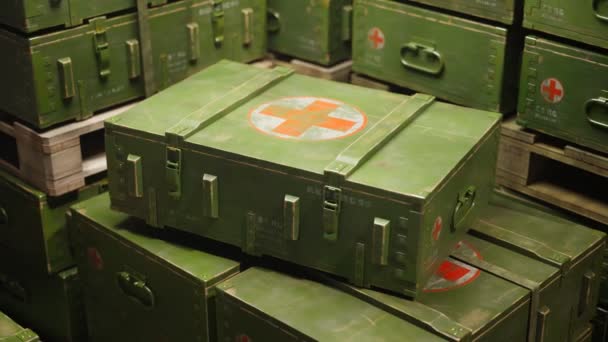 上の赤十字のいくつかの緑の箱は木パレットの上に積み重ねられています 真ん中の明るい光で一つの箱がハイライトされています 箱には軍事目的のための医療用品が含まれています — ストック動画
