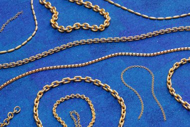Altın zincir koleksiyonu. 3 boyutlu sergiler, çeşitli karmaşık tasarımlarda, göz kamaştırıcı, gerçekçi altın kolyeler sergiliyor. Kolyeler koyu mavi bir arkaplana göre dizilmiş..