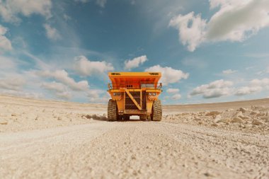 Sarı damperli kamyon taş ocağından geçiyor. Ağır bir yük taşıyan devasa endüstriyel makineler. Kuru, tozlu hava ve kazı alanında güneşli hava..