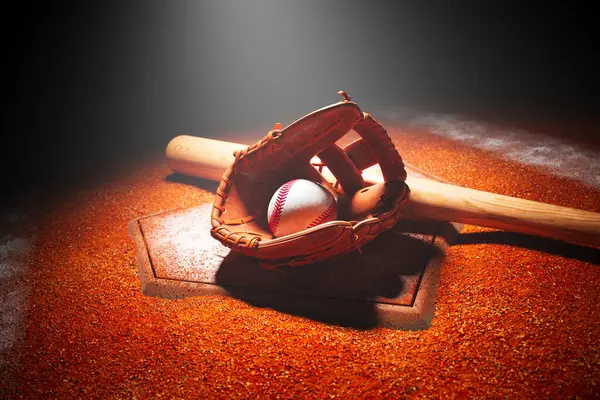 Baseball leather glove, ball, and bat on a dirty white base with a dark stadium as the background. White base lines and orange gravel dirt are visible.