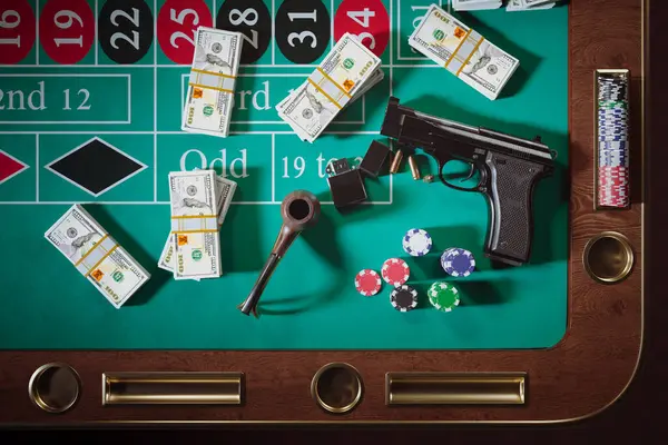Guns with bullets, money and chips on a roulette table in a casino. Gambling. Gangster weapon next to wads of cash, pipe with firestarter. Concept of danger play. Crime in Vegas. Risky entertainment.