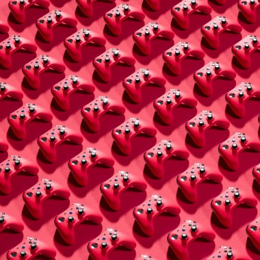 Kırmızı arka plandaki ızgara deseninde düzgünce dizilmiş sonsuz sayıda kırmızı oyun denetleyicisinin görüntüsü. Oyun, teknoloji ve eğlence kavramlarını resmetmek için mükemmel.