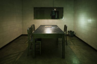 Metal masası, sandalyeleri ve yarı saydam aynası olan sorgu odası, kelepçeler ve görünen dosyalar. Bir şüpheliyi sorgulamak ve duygularını gözlemlemek için mükemmel bir yer..