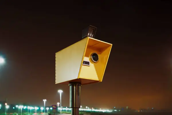Speed camera takes photos with the flash at night. Speed control at the road. City lights in the dark background. Speed limit. Slow down. Speedometer takes measurements of cars\' acceleration. Close up