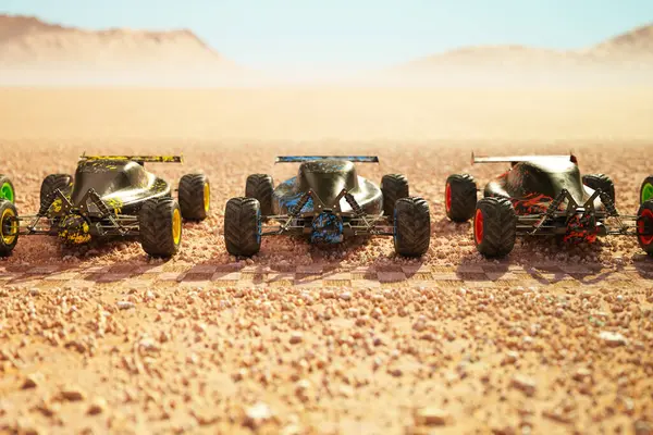 Multiple colourful remote-controlled buggy cars on a start line in the desert ready for the race. Hot, sunny day and dry sand race track. Mountains and dust cloud in the distance. Front view.