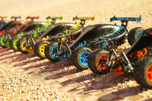 レースの準備ができている砂漠のスタートラインで列に待っている複数のカラフルなリモートコントロールバギー車 おもちゃサーキットが始まりました 暑くて晴れた日と乾燥した砂のレースコース サイドビュー — ストック写真