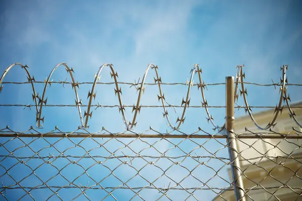 写真は刑務所のフェンスを眺めながら 散歩中の囚人の視点を捉えています イメージは 投獄と限られた自由の厳しい現実を示しています カメラは有刺鉄線に焦点を当てています — ストック写真