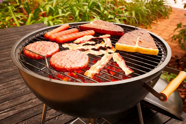 Grill at the garden terrace. Traditional American barbeque. Crispy steaks, sausages, bacon and burgers. Grilling delicious meat. Preparing a tasty meal. Unhealthy food. Hot grilled meat. Dinner time
