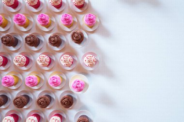 Zengin çikolata ve kremalı vanilya aromalı, pembe ve kahverengi şekerle süslenmiş, el değmemiş beyaz bir yüzeyde zarif bir şekilde sunulan çeşitli kapkek koleksiyonu..