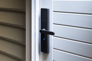 Bir evin beyaz kapısındaki gelişmiş elektronik akıllı kilidin yakın çekimi. Güvenli, anahtarsız giriş ve modern kolaylık için tuş takımı içeriyor..