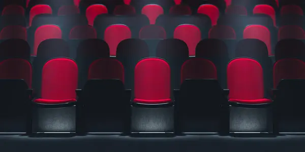 在聚光灯下 只有一个红色的剧场座位 在黑暗的电影院里 在一排排空荡荡的黑色椅子之间显得格外醒目 使人产生一种期待感和独占感 — 图库照片