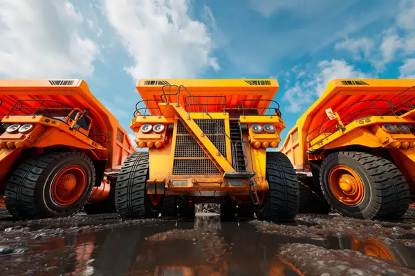 鉱山作業のために設計された巨大なオレンジダンプトラックのペアは 強化されたタイヤと明確なヘッドライトで明確に表示され オープンマインの設定で頑丈な作業のためにポット — ストック写真