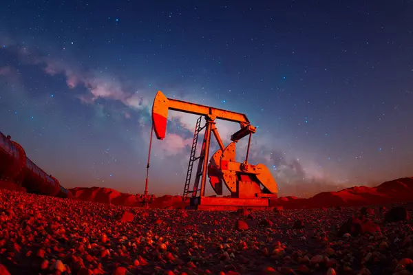 夜のキャンバスに身を包んだオイルポンプジャックは 広大な星明かりの空の下で石油をリズム的に抽出し 産業力と天然資源の搾取を象徴しています — ストック写真