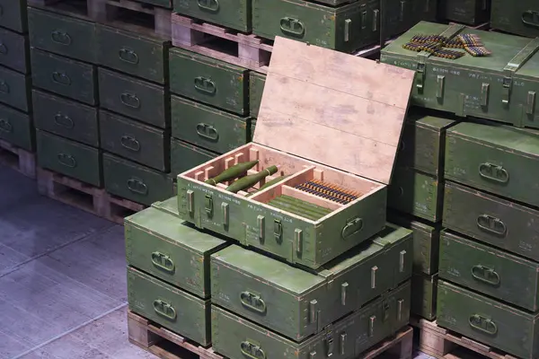 A neatly arranged collection of green military ammunition boxes on wooden pallets, with one container open, showcasing a variety of shells and bullets in a secure depot setting.