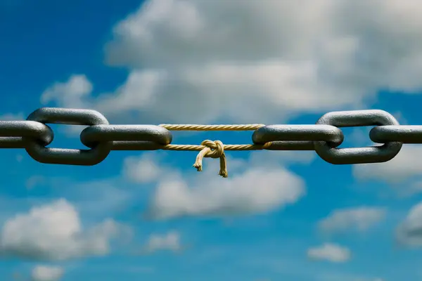 A symbolic high-contrast image capturing the silhouette of a steel chain link intertwined with a knotted rope against a backdrop of a cloudy sky, illustrating themes of challenge and connection.