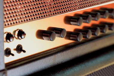 Bağbozumundan esinlenilmiş gitar amplifikatörünün dokusunu ve detaylı tasarımını gösteren, kontrol düğmelerini ve imza ızgara desenini vurgulayan karmaşık bir yakın çekim..