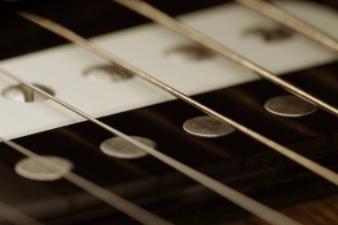 Ses deliğine ihtişamlı bir şekilde yayılmış akustik gitar tellerinin detaylı dokusunu ve zanaatkarlığını gösteren karmaşık bir makro fotoğraf..