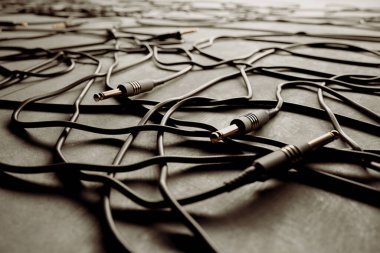 Birbirine dolanmış karmaşık ses kabloları ve 3.5 mm 'lik krikolar dağınık bir şekilde, düzensiz bir karmaşıklığın altını çizerek, gri bir zemin üzerinde ayrıntılı bir ağ oluşturuyorlar..