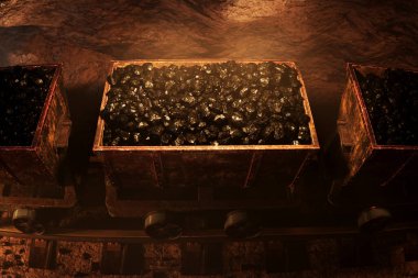 Kömür çıkarmanın özünü yakalayan resim: raylarda üç yüklü araba, enerji üretimi ve sanayi sektörlerinde kömürün kilit rolünü gözler önüne seriyor.