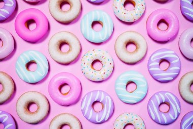 Bu resim çeşitli rengarenk malzemelerle donutları yakalar. Pembe bir arkaplanda, tatlı veya fırın teması için mükemmel bir şekilde düzenlenmiştir..