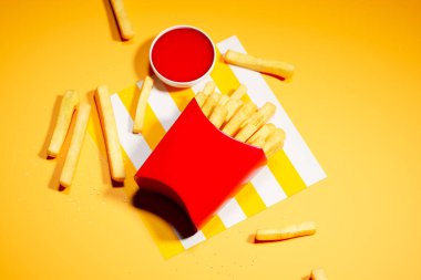 Büyüleyici bir minimalist kompozisyonda canlı kırmızı bir ketçap kutusunun yanına serpiştirilmiş gevrek patates kızartmaları bulunur..