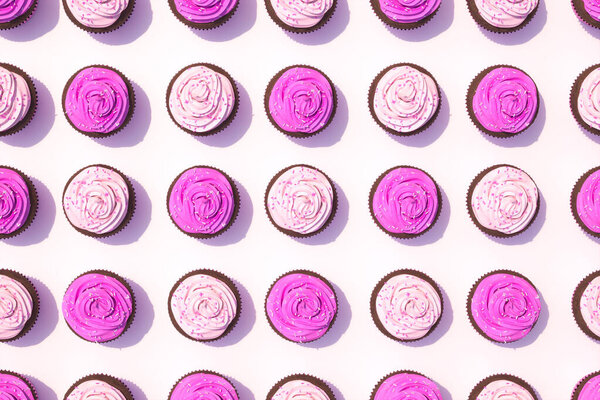 Захватывающий дисплей с шоколадными кексами, украшенными ярко-розовой глазурью и красочными посыпками, представленными на белом фоне.