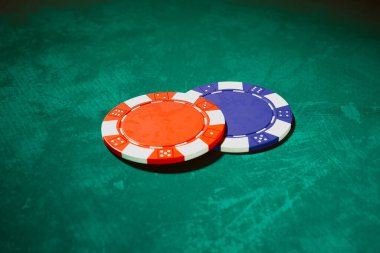 This image captures striking red and blue poker chips positioned on a rich green felt surface, evoking the intense atmosphere of gambling and strategic play in a casino setting. clipart