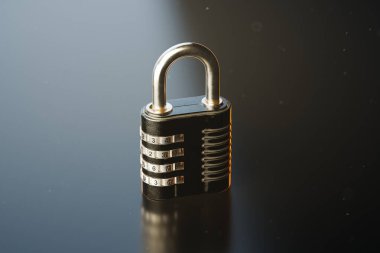 Bu resim, gümüş sayısal kadranların yer aldığı, güvenlik ve gizliliği simgeleyen parlak siyah bir arkaplan üzerine kurulmuş bir asma kilidin ayrıntılı yakın çekimini yakalar..