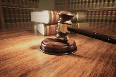 A polished wooden gavel lies on the judge's bench with a backdrop of law books, encapsulating the essence of judicial authority and the legal system. clipart