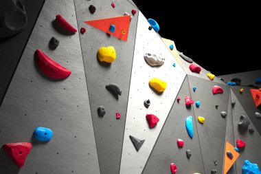 Canlı ve geometrik şekilli tutmalarla bezenmiş, dokulu gri tırmanma duvarının çekici yakın çekimi, eğlenceli ve zindelik yarışması sunuyor..